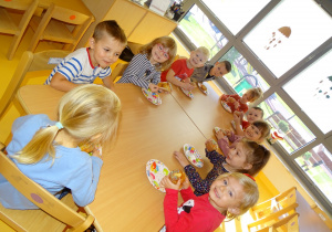 06 Dzieci siedzą przy stole i jedzą babeczki na kolorowych talerzykach